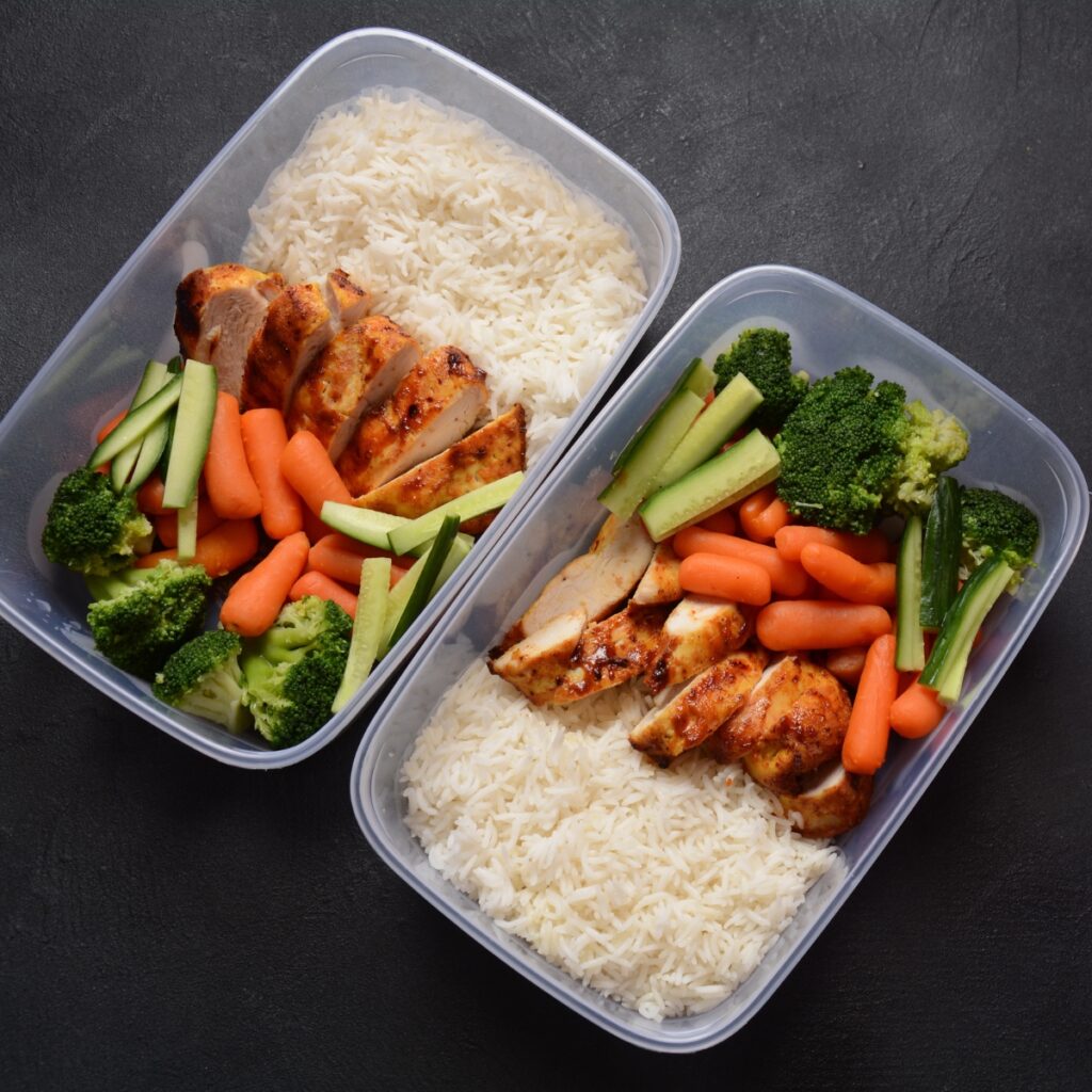 Rectangle boxes of rice with sliced chicken, carrots and broccoli.