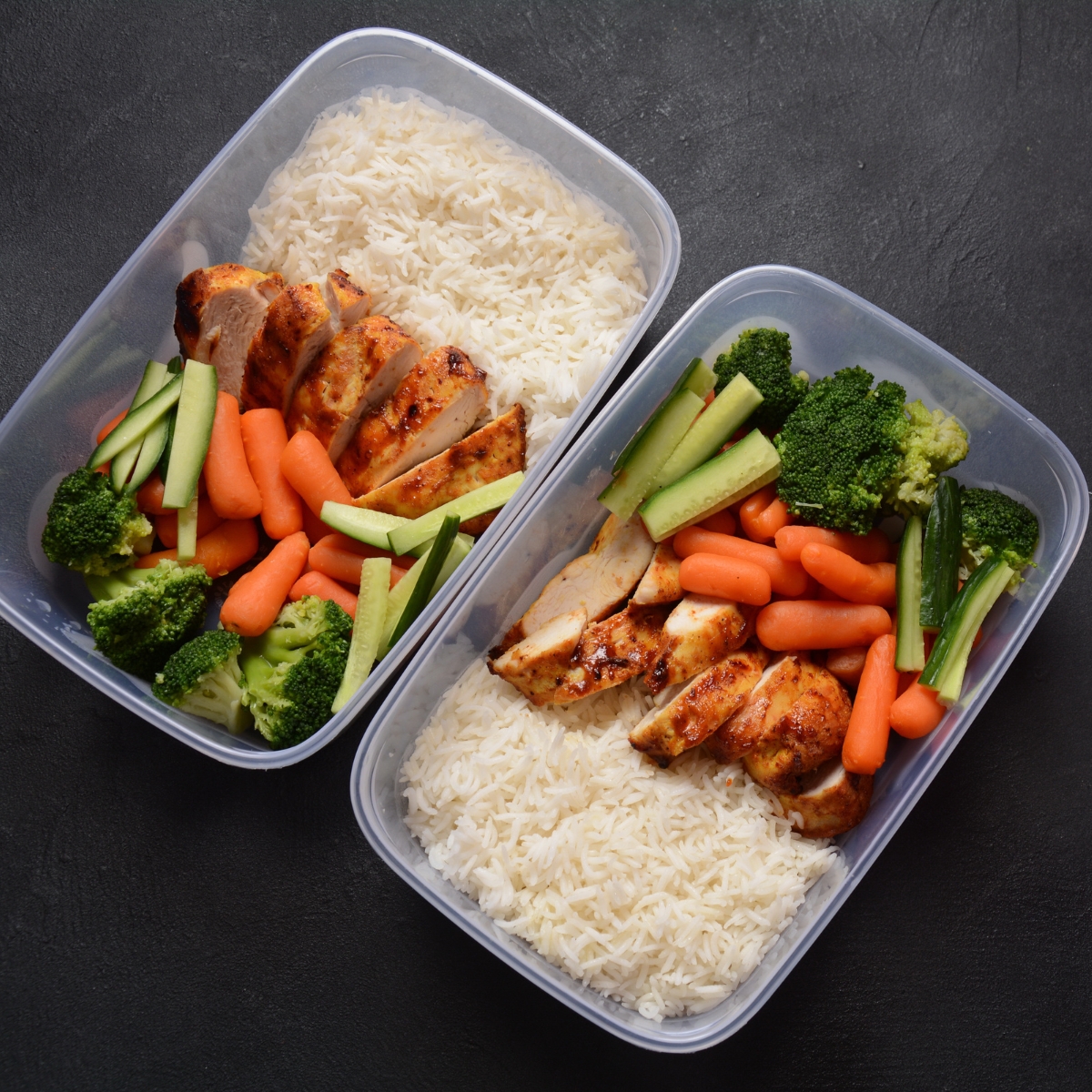 Rectangle boxes of rice with sliced chicken, carrots and broccoli.