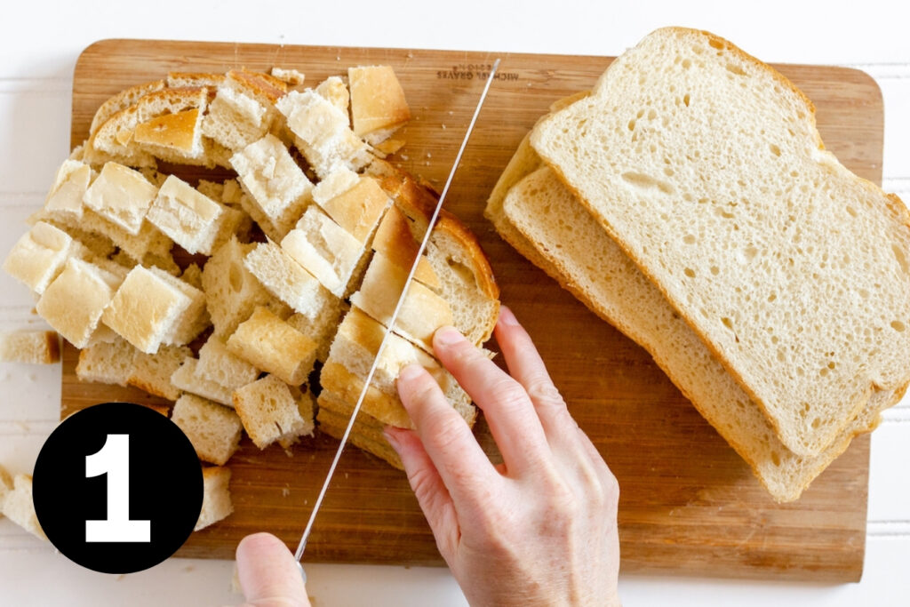 Bread being diced on a cutting board with a long bread knife.